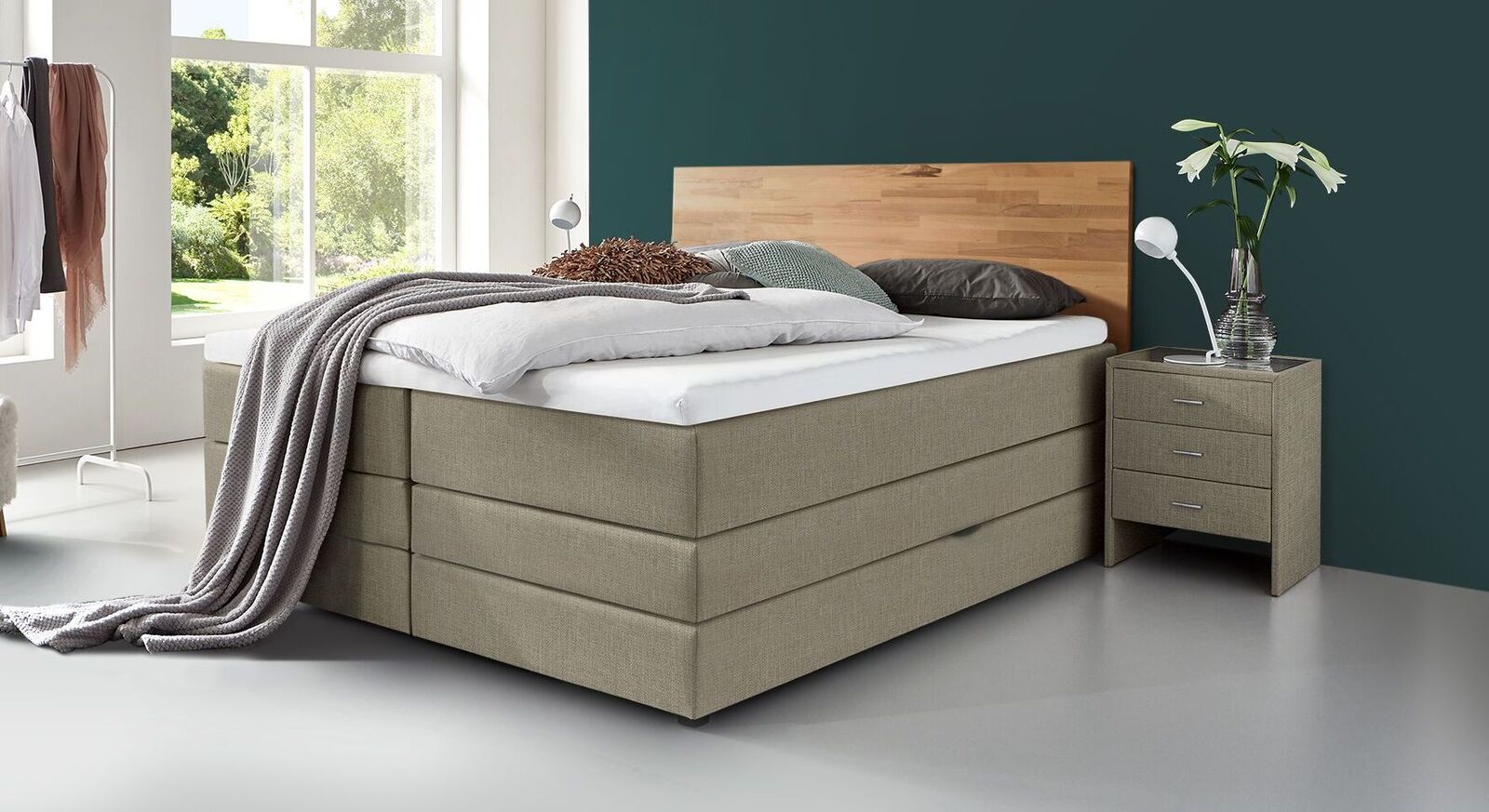Klassische Kombination: das Bettkasten-Boxspringbett "Peachland" mit Holz-Kopfteil und graubeige meliertem Webstoffbezug.