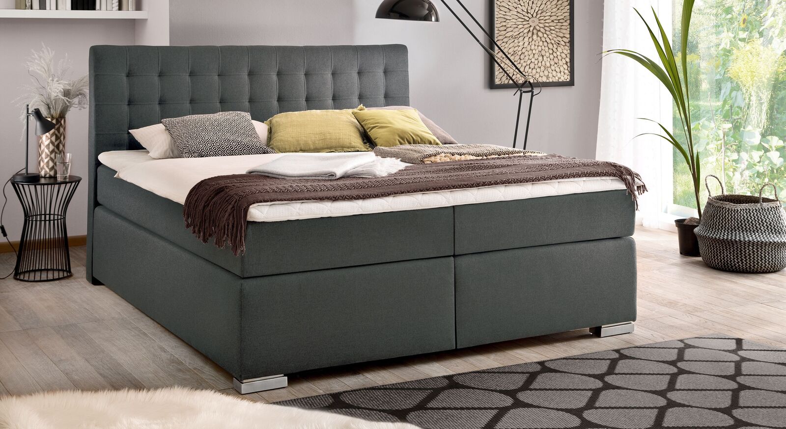 Das Bettkasten-Boxspringbett "Santera" (hier in Webstoff grob, anthrazit und mit Metallfüßen) lässt sich in viele Einrichtungskonzepte integrieren.