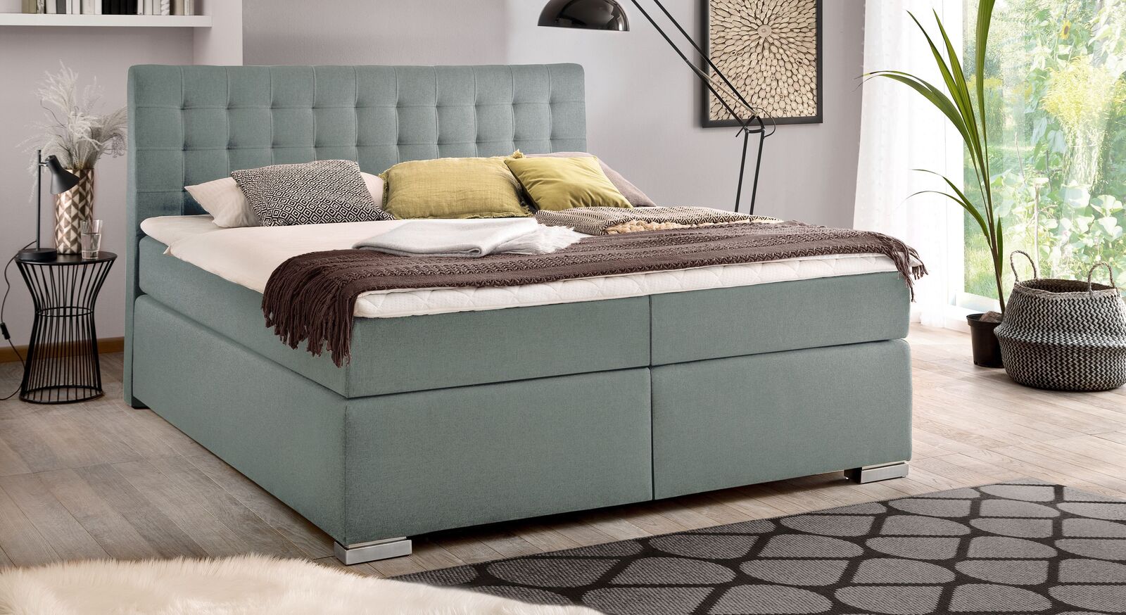 Einen modernen Charakter erhält das Bettkasten-Bett "Santera" mit dem eisblauen Webstoffbezug.