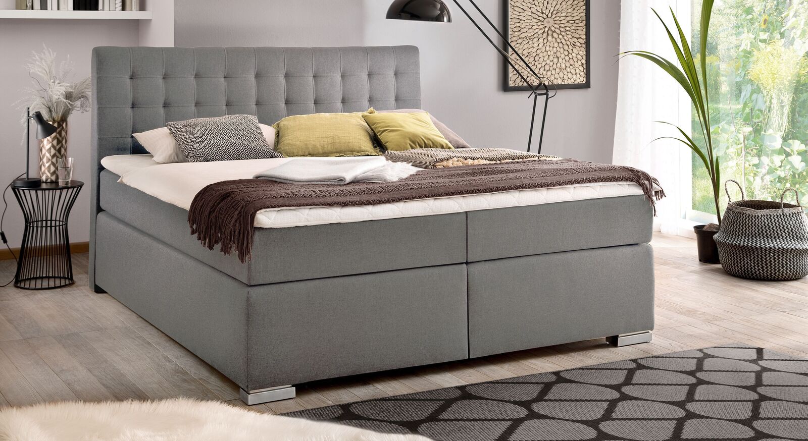 Im unsichtbaren Bettkasten des Boxspringbettes "Santera" (hier in feinem hellgrauen Webstoff und mit Metallfüßen) verstauen Sie Dekokissen und Decken.