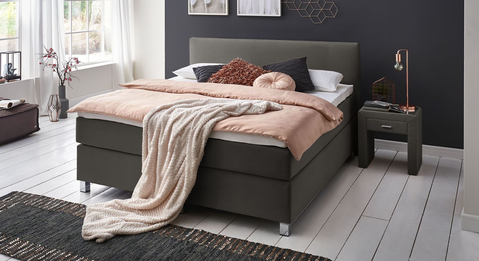 Der anthrazitfarbene Webstoff des 66 cm hohen Boxspringbettes harmoniert hervorragend mit den Füßen.