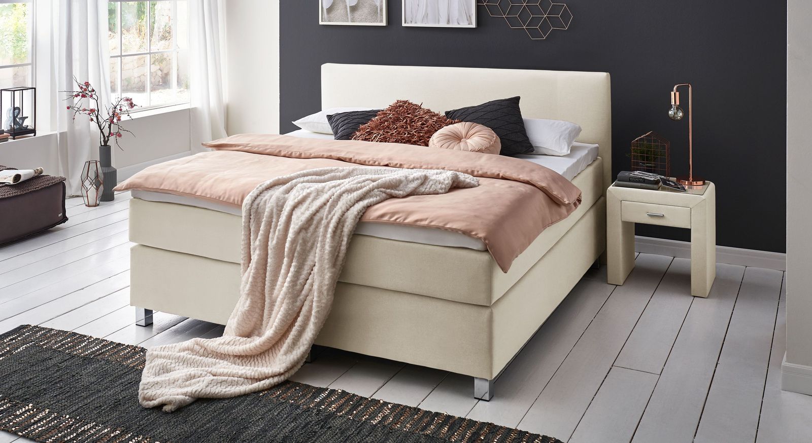 Das cremefarbene Boxspringbett "Ferryland" ist hier mit einer Liegehöhe von 66 cm abgebildet.