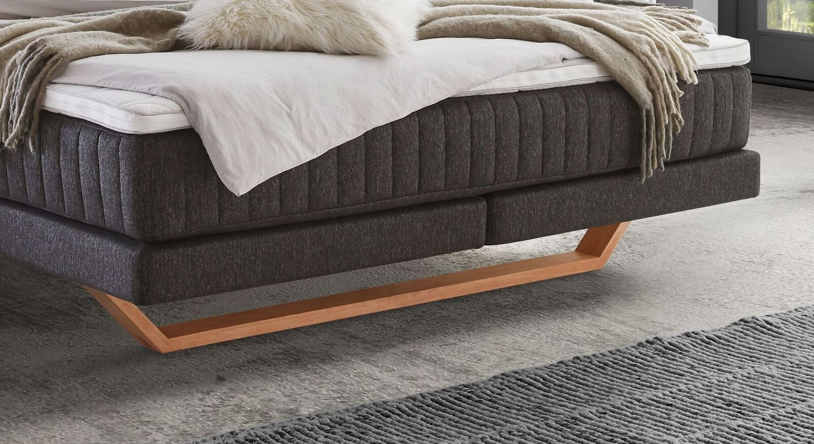 Seinen stabilen Stand erhält das attraktive Boxspringbett durch markante Kufen aus naturfarbenem Eichenholz.