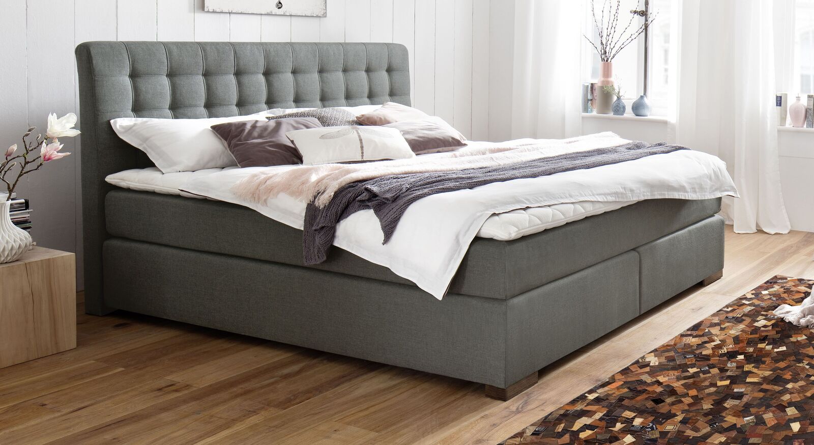 Im Boxspringbett "Matai" (hier in Grau mit Holzfüßen) verbringen Sie gemütliche Fernseh- und Leseabende.