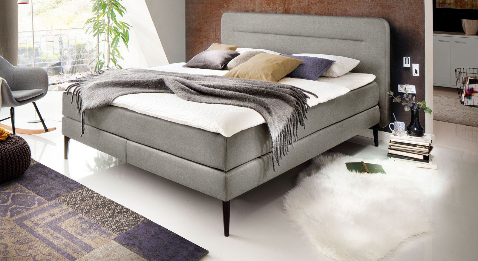 Klassisch elegant: das Boxspringbett "Paroldo" – hier in hellgrauem Webstoff mit schwarzen Füßen und ohne Unterleisten.