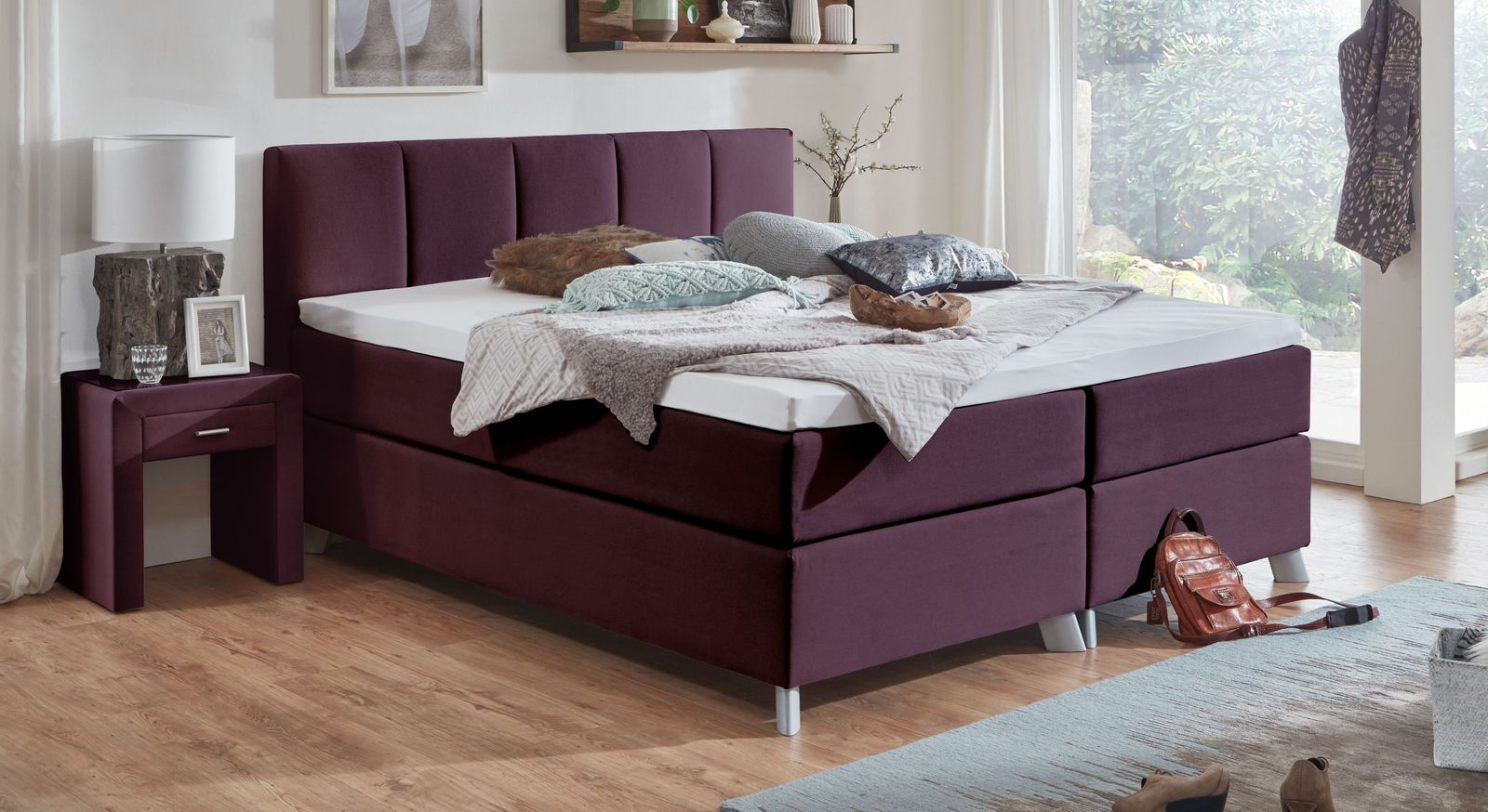 Das 66 cm hohe Boxspringbett "Ramea" ist hier in einen edlen beerefarbenen Webstoff gehüllt.