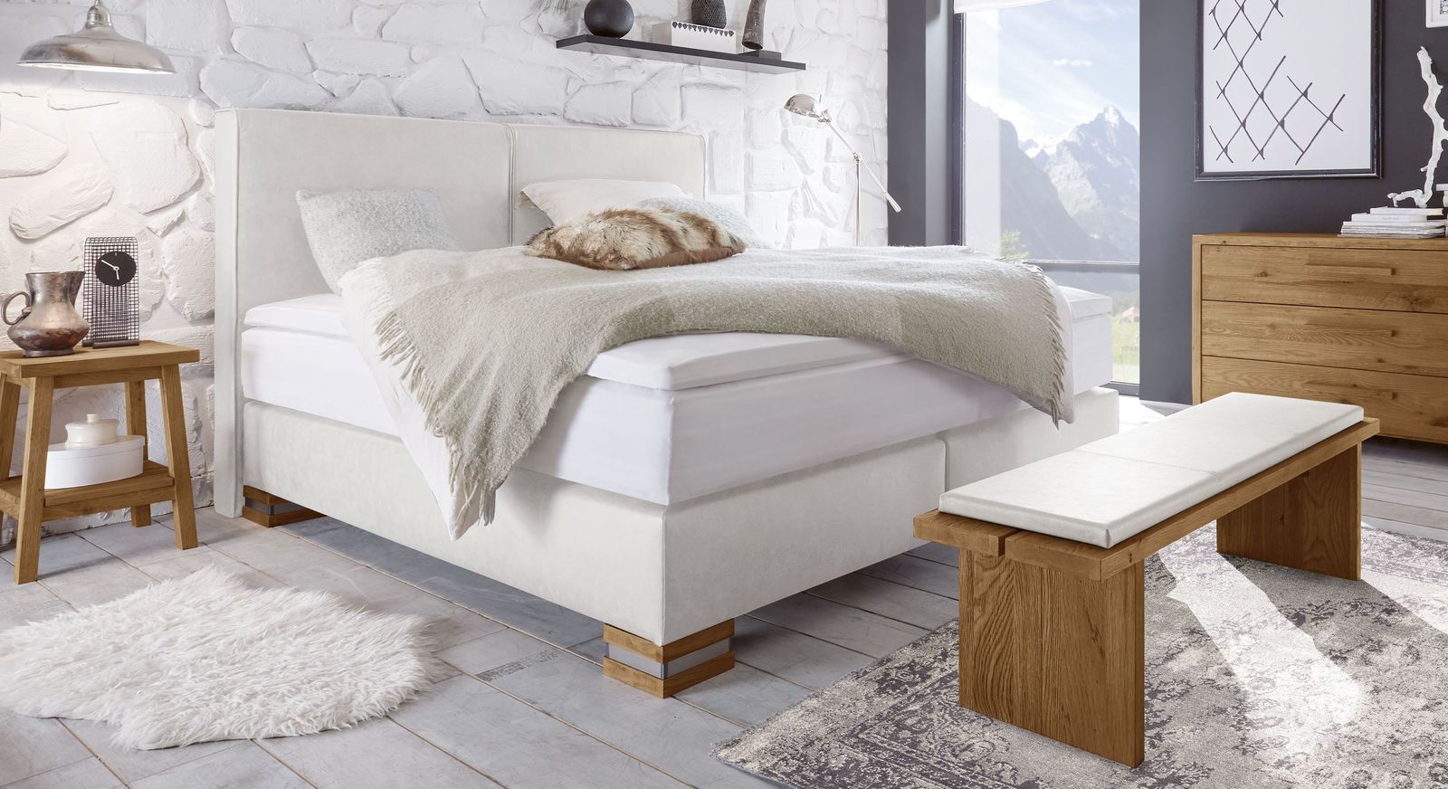 Dezente Eleganz strahlt das Boxspringbett "Tholen" in weißem Kunstleder mit Füßen in Wildeiche natur aus.