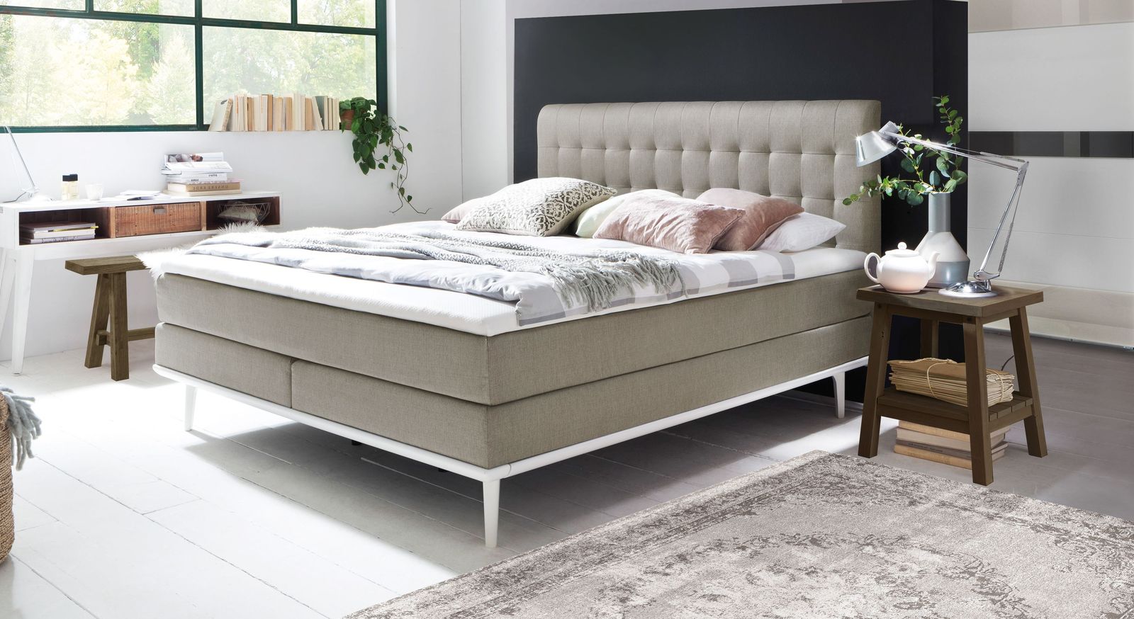 Verleihen Sie Ihrem Schlafzimmer mit dem Boxspringbett (hier in Hellgrau mit weißen Füßen und Unterleisten) ein elegantes Flair.
