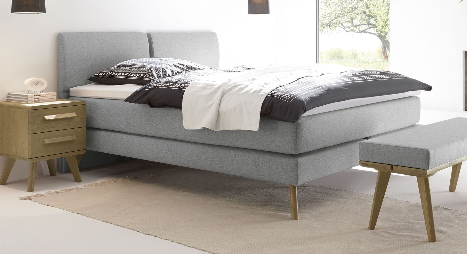 Klassische Eleganz strahlt das Doppelbett im Retrolook mit einem weißgrauen Fischgrät-Veloursbezug aus.