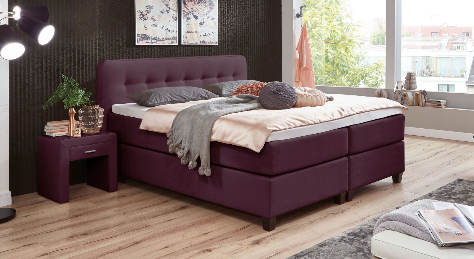 Modern und einladend: das hohe Boxspringbett "Westport" im beerefarbenen Webstoff.