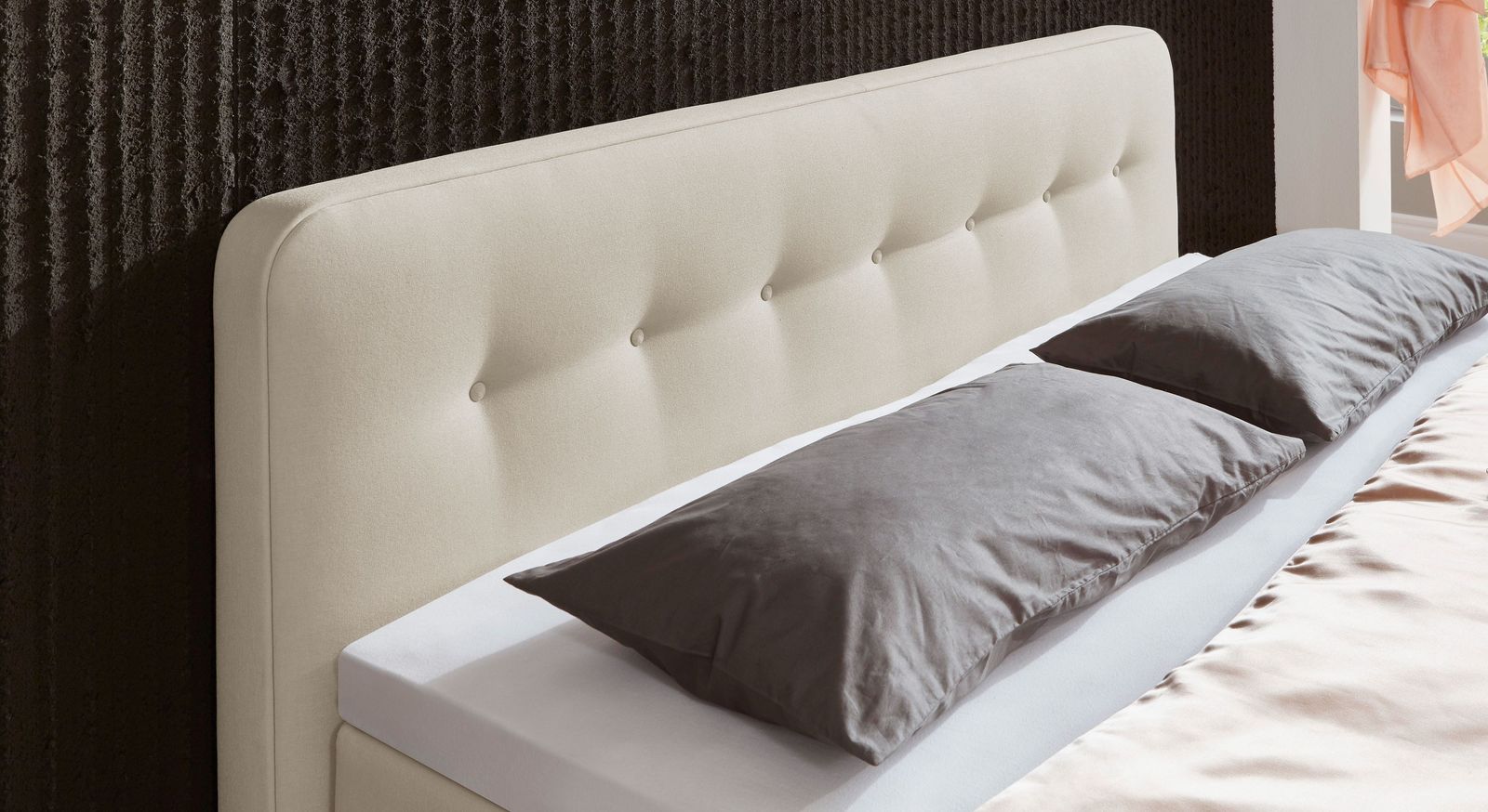 Ansprechende Knopfheftungen zieren das hohe aufgepolsterte Kopfteil des Boxspringbettes.