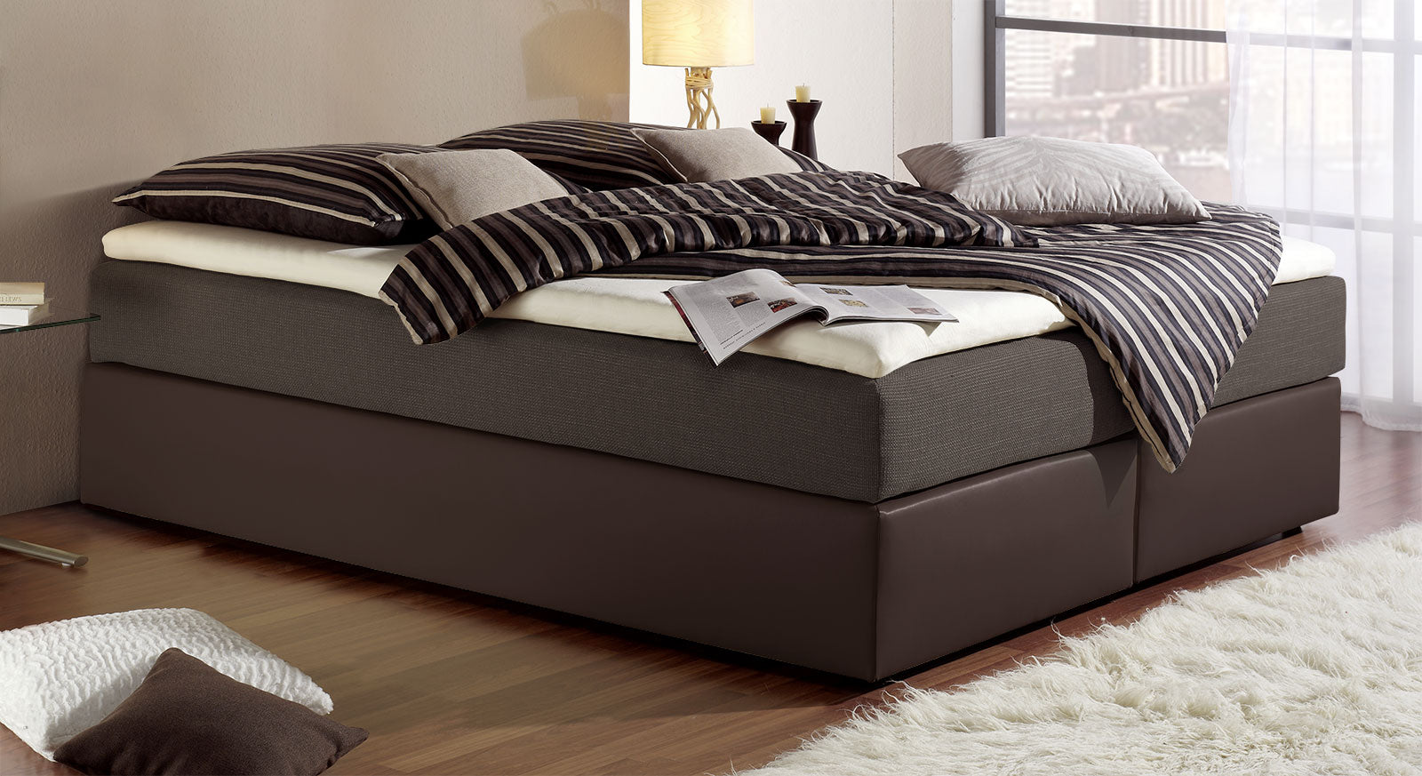 Dunkelbraunes Kunstleder und braunbronzener Stoff kleiden hier die Boxspringliege "Sydney".