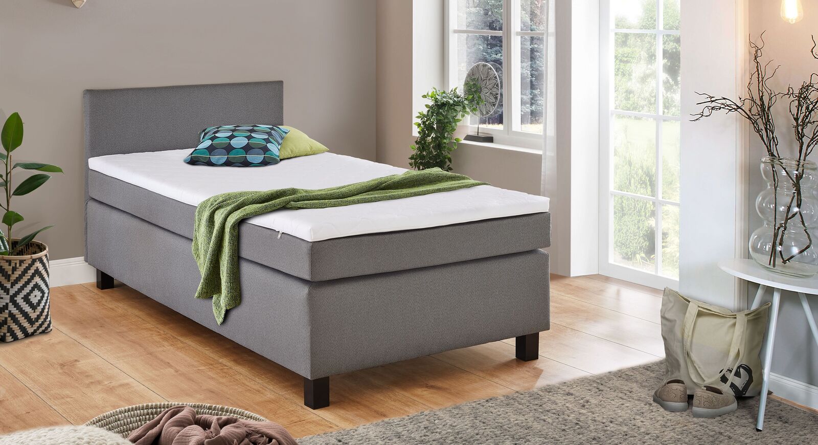 Preiswert und perfekt f&uuml;r kleinere R&auml;ume: das Boxspring-Einzelbett "Lucan" mit silbergrauem Webstoffbezug und schwarzen Bettbeinen.
