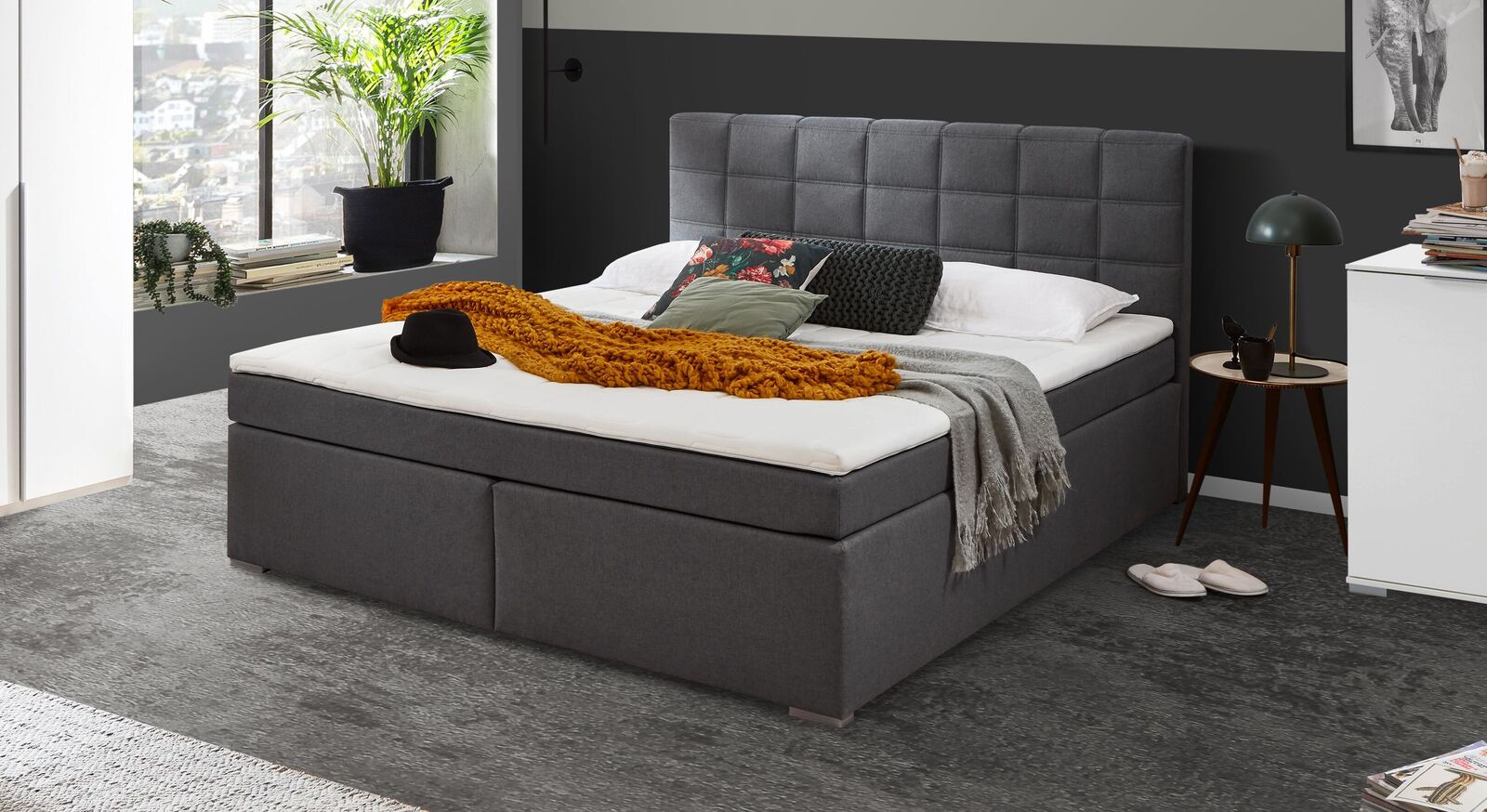 Das Boxspringbett "Arcadius" begeistert mit seinem gesteppten Kopfteil, das mit grauem Webstoff bezogen ist.