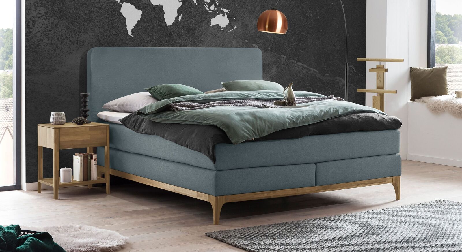 Das elegante Boxspringbett "Conrado" (hier in Blaugrau) steht auf einem stabilen Sockel aus massivem Eichenholz und ist mit Fischgr&auml;t-Velours bezogen.