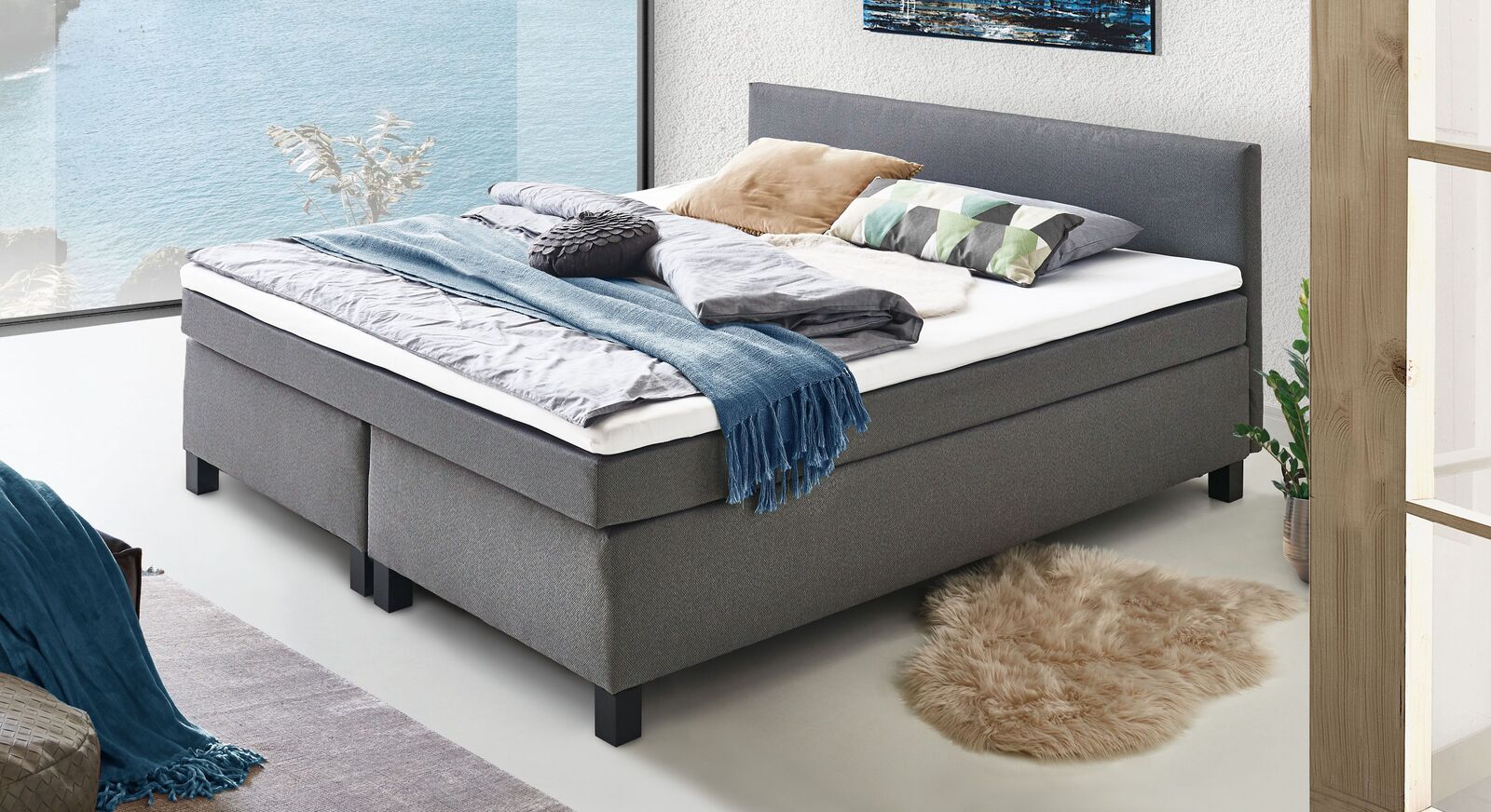 Das preiswerte Boxspringbett "Lucan" ist mit silbergrauem Webstoff bezogen und wird inklusive Box, Matratze und Topper geliefert.