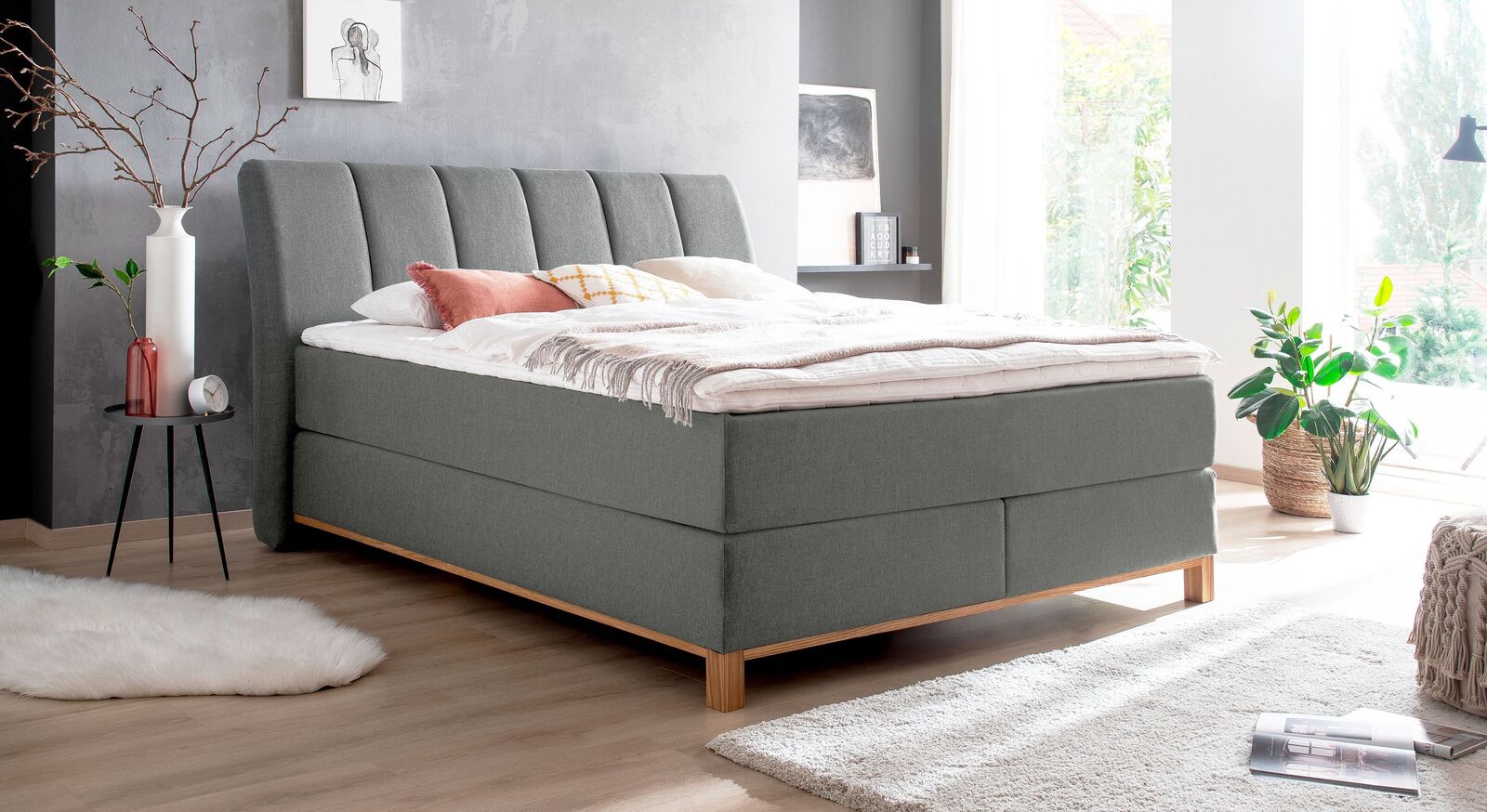 Stilvolle Eleganz f&uuml;r Ihr Schlafzimmer: das Boxspringbett "Rivelino" (hier in Grau) mit Massivholz-Unterbau und gestepptem Kopfteil.