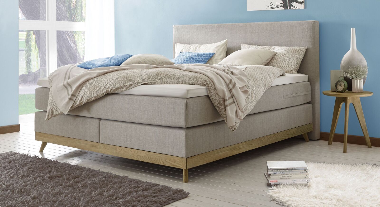 Gem&uuml;tlich und schick im Scandi Style: das Boxspringbett "Sivar" (hier in Hellgrau) mit weichem Webstoffbezug und stabilen Sockel aus Massivholz.