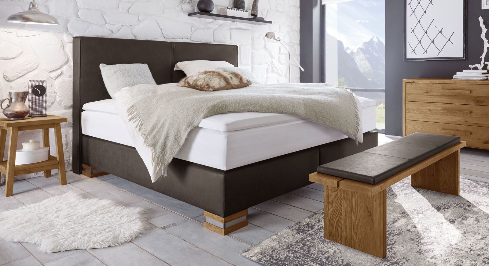 Nat&uuml;rliche Farbvariante: das Boxspringbett in dunkelbraunem Luxus-Kunstleder mit F&uuml;&szlig;en in Eiche natur.