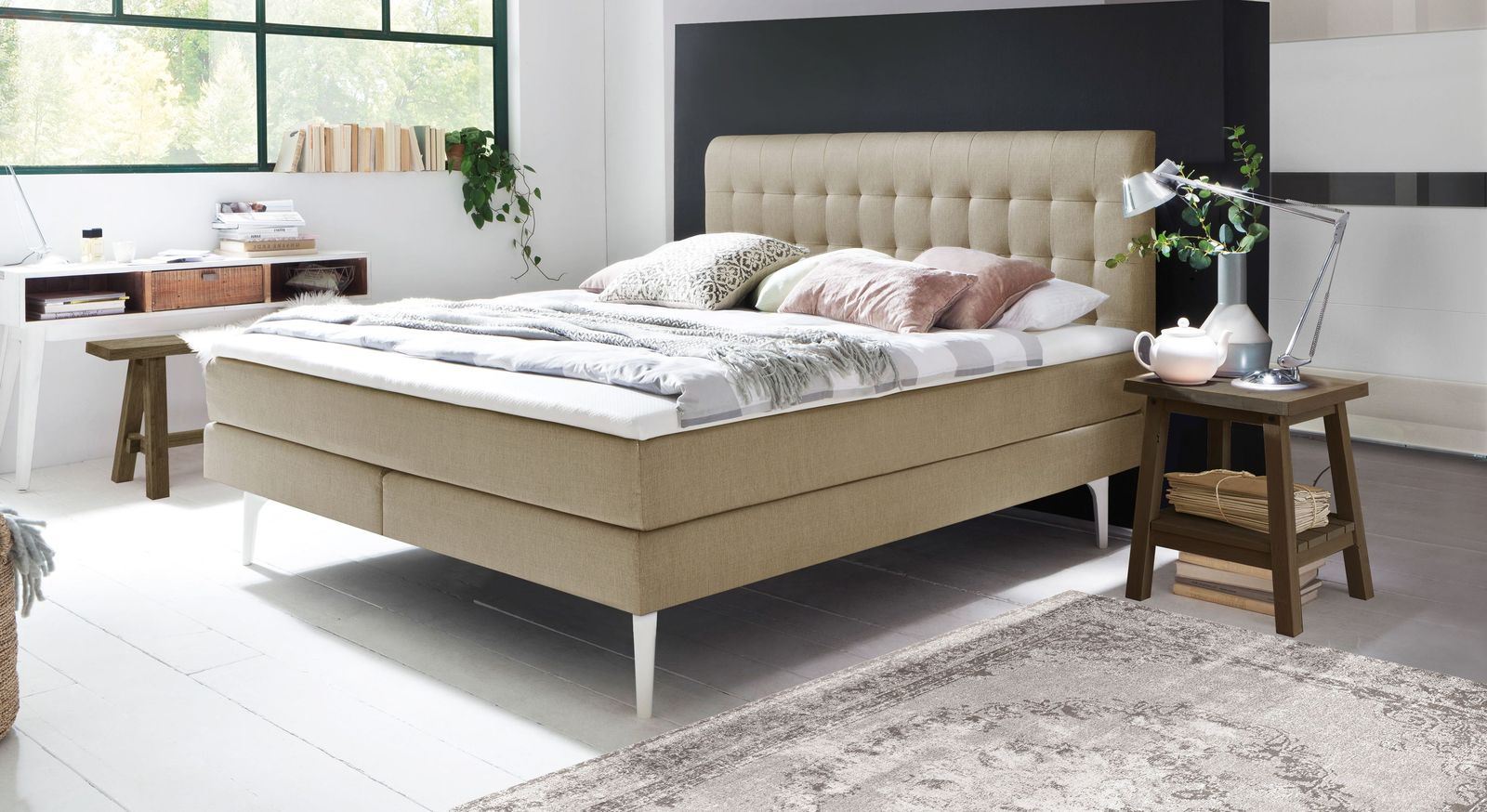 Filigran wirkt das Boxspringbett "Tromello" ohne Unterleisten (hier in Beige mit wei&szlig;en F&uuml;&szlig;en).